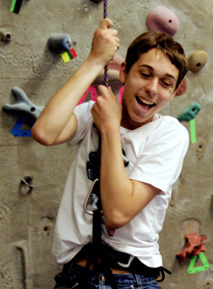 A young boy clings to a rope while climbing a rock wall