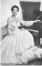 A woman wearing a white dress sits at a piano