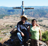 A man and woman in front of a wooden cross atop a mountain